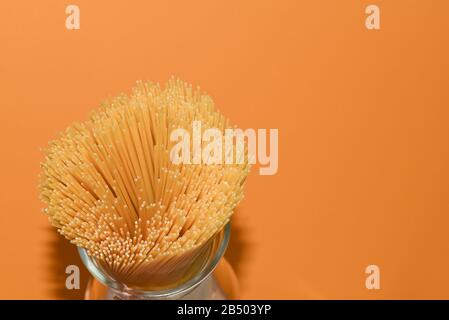 view from above on a yellow spaghetti in a glass jug on an orange background with copy space, shooting with flash hard light, bunch of thin straws Stock Photo