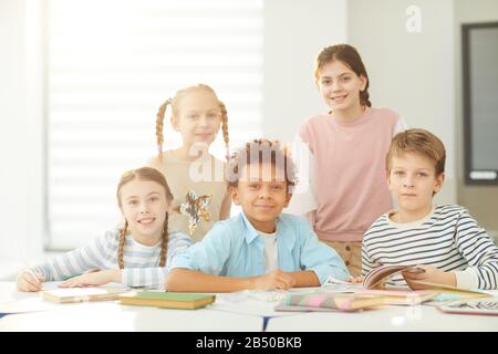 Portrait of smart boys and girls sitting and standing together in modern classroom looking at camera, horizontal shot, copy space Stock Photo