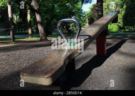 wooden seesaw for two with metal handles on an empty playground in a summer park, image on the topic of child protection, abducted or missing children Stock Photo