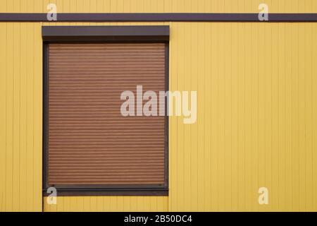 window with a brown steel protective roller shutter on a yellow building facade, background for design and copy space for text Stock Photo