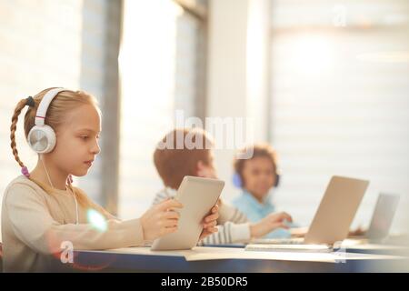 Middle school students sitting in classroom using modern headphones and computers during lesson, horizontal shot, copy space Stock Photo