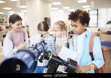 Group of four curious children using modern school telescope to look at sky, horizontal shot Stock Photo