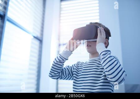 Horizontal medium low angle portrait of unrecognizable ten-year-old Caucasian boy using VR headset, copy space Stock Photo