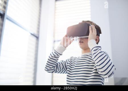 Horizontal medium low angle portrait of unrecognizable ten-year-old Caucasian boy using VR headset, copy space Stock Photo