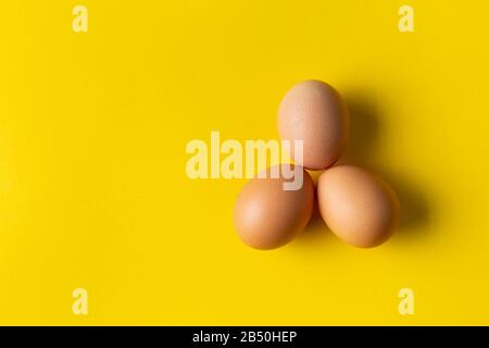 Three eggs on yellow background. View from above. Stock Photo