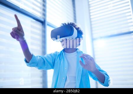 Horizontal low angle shot of unrecognizable middle schooler using VR headset pointing finger at something, copy space Stock Photo