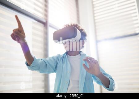 Horizontal low angle shot of unrecognizable middle schooler using VR headset pointing finger at something, copy space Stock Photo