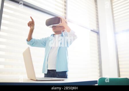 Horizontal low angle medium long shot of unrecognizable boy using VR headset pointing finger at something, copy space Stock Photo