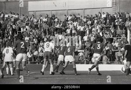 1970s, historical, fans watching a football match standing on the terraces, at Millwall, FC, South London, England, UK. Football terraces are a number of concrete steps with metal barriers installed at numerous locations to prevent people moving down the slope. Stock Photo