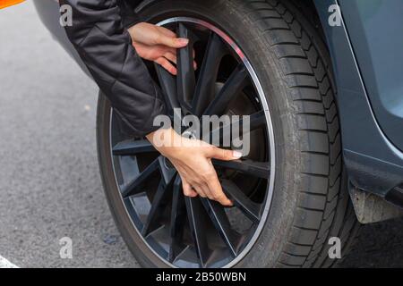 Woman is changing a wheel in broken car on the road. Closeup womans hand on the wheel of a vehicle. Stock Photo