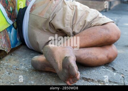 Poor homeless man sleeping on the wooden bench on the urban street in the city. Stock Photo