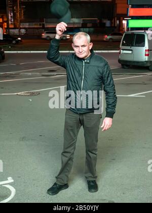 A man with a baseball cap in his hands at night on the street. People background image. Father's day. Place for text. Grey hair. Stock Photo