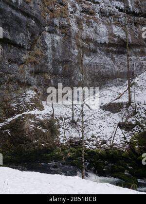 Impressive cliff and the Orbe river at the Villorbe Caves in the Jura Mountains in Vallorbe, Switzerland. Icicles hanging from the cliff edge. Stock Photo