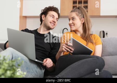 Couple using fast home internet with laptop and digital tablet. Woman and man on sofa in living room Stock Photo