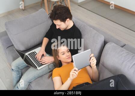 Couple using fast home internet with laptop and digital tablet. Woman and man on sofa in living room Stock Photo