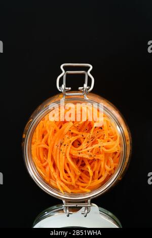 500 grams of spicy korean carrot salad with oil, garlic and black pepper in glass jar. Sustainable packaging, black background, high resolution Stock Photo