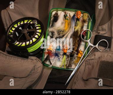 Still life composition of fly fishing equipment including a vest, reel, forceps and fly box Stock Photo