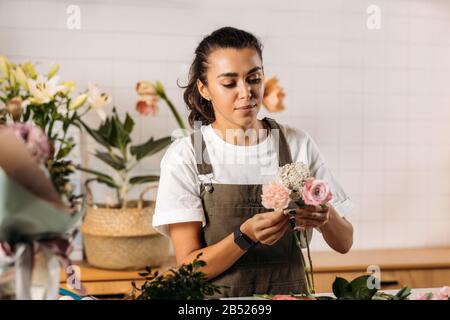 Woman standing at table making a bouquet of fresh flowers. Female florist working in flower shop. Stock Photo