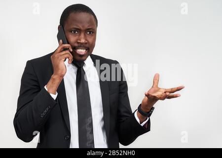Closeup of angry young african man screaming while talking on smartphone over grey background Stock Photo