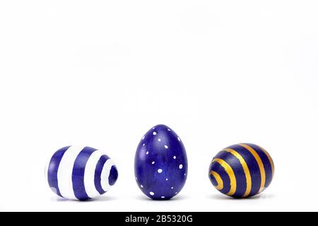 Three easter eggs trendy colored classic blue, white and golden decorated on white table. Happy Easter card with copy space for text. Minimal style Stock Photo