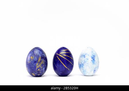 Three easter eggs trendy colored classic blue, white and golden decorated on white table. Happy Easter card with copy space for text. Minimal style Stock Photo