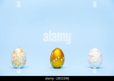 Three easter trendy golden decorated eggs on blue background. Happy Easter card with copy space for text Minimal easter style Stock Photo