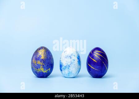 Three easter trendy colored classic blue, white and golden decorated eggs on blue. Happy Easter card with copy space for text. Minimal style. Stock Photo