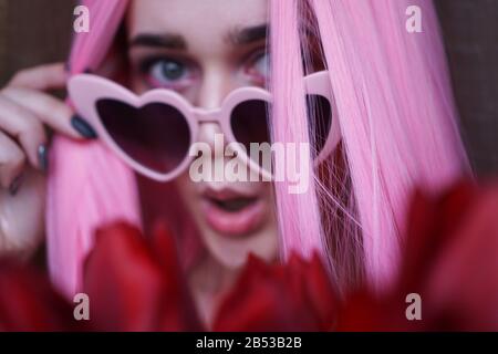 Surprised woman with tulip flowers - Pink hair and heart-shaped glasses - Out of focus, blurred background Stock Photo
