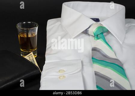 folded white shirt with green and silver striped necktie and shot of whiskey and wallet on black Stock Photo