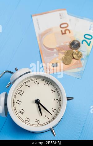 Analog classic alarm clock on a blue wooden background with euro bills and cents. Loan and tax concept Stock Photo