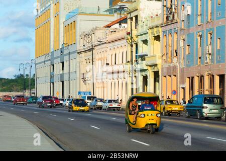Traffic of vehicles including tuk tuk (coco taxi) in front of colonial style building. View of the promenade called Malecón in Havana, Cuba. Stock Photo