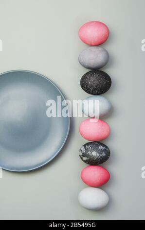 Line of colorful Easter eggs near blue plate on grey background. Minimalistic flat lay Stock Photo