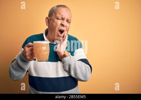 Senior handsome man drinking jar of beer standing over isolated yellow background touching mouth with hand with painful expression because of toothach Stock Photo