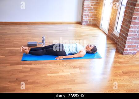 Middle age beautiful sportwoman lying down on mat practicing yoga doing corpose pose at gym Stock Photo