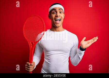 Young handsome african american sportsman playing tennis using racket over red background very happy and excited, winner expression celebrating victor Stock Photo