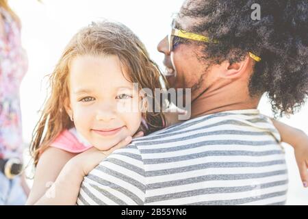 Happy multiracial family having fun on the beach - Young daughter hugging her father in summer vacation - Love, tender moments, holidays and parents l