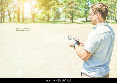 Young cheerful man using a drone with remote controller - Blond trendy guy having fun with new aerial technology trends - Focus on face and hands - Wa Stock Photo