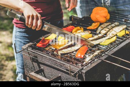 Young woman cooking organic vegetables at barbecue dinner outdoor - Couple grilling peppers and aubergines for vegan bbq - Vegetarian and healthy life Stock Photo