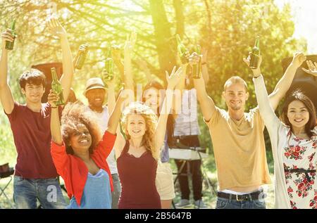 Multiracial young friends dancing in garden party with deejay in background - Cheerful people holding bottle beers on barbecue weekend day - Friendshi Stock Photo