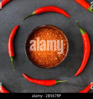 Flat lay of Thai red fresh hot chilli peppers with green tails and dried red chilli flakes in bowl on black stone background. Food pattern. Popular sp Stock Photo