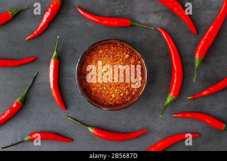 Flat lay of Thai red fresh hot chilli peppers with green tails and dried red chilli flakes in bowl on black stone background. Food pattern. Popular sp Stock Photo