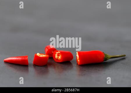 Red chilli pepper with sliced on black stone background, soft focus, free space. Spicy capsicum pepper wallpaper pattern Stock Photo