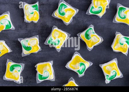 Close up of yellow ang green capsules with laundry detergent and dishwasher soap on black stone background, flat lay, Stock Photo