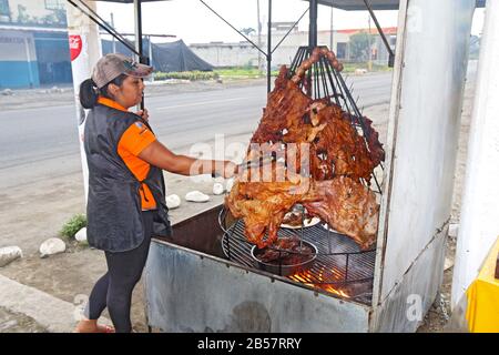 Woman tends to meat roasting over a fire at a restaurant at the side of the main road through the city of Naranjal in ecuador. Stock Photo