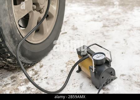 Pump, automobile compressor for inflating tires with air stands in the winter on the snow and pumps the flat tire of the car Stock Photo
