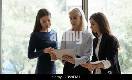 Diverse female colleagues brainstorm working on tablet in office Stock Photo