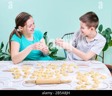Mom teaches son to sculpt dumplings with cottage cheese in the kitchen. Stock Photo