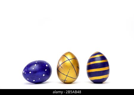 Three easter eggs trendy colored classic blue, white and golden decorated on white table. Happy Easter card with copy space for text. Minimal style Stock Photo