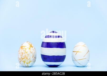 Three easter trendy colored classic blue and golden decorated eggs on blue background. Happy Easter card with copy space for text Minimal easter style Stock Photo