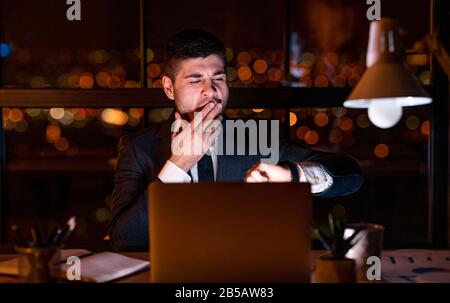 Businessman Yawning Checking Time Working Late At Night In Office Stock Photo